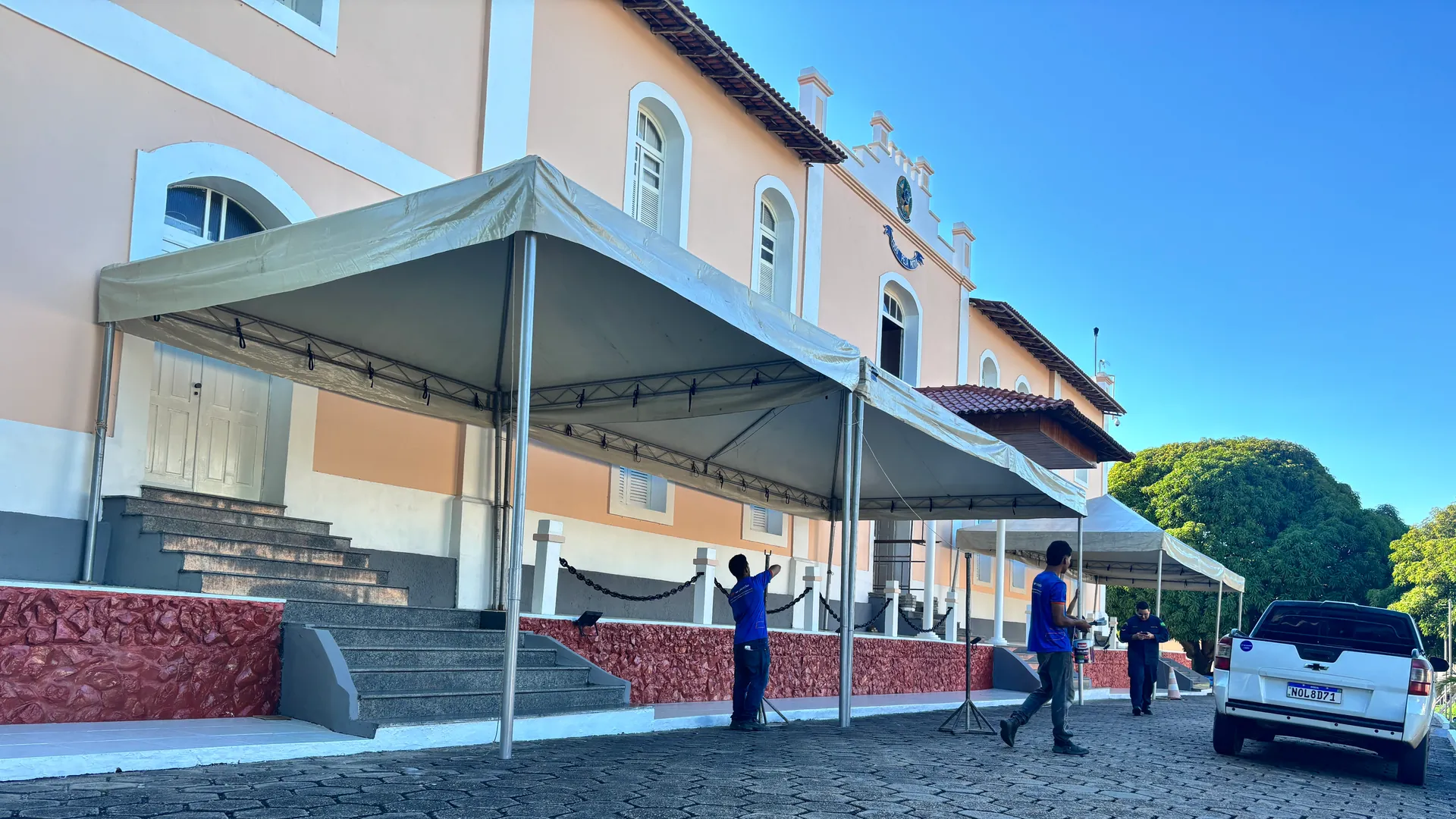 Equipe montando tendas brancas em frente a um edifício histórico